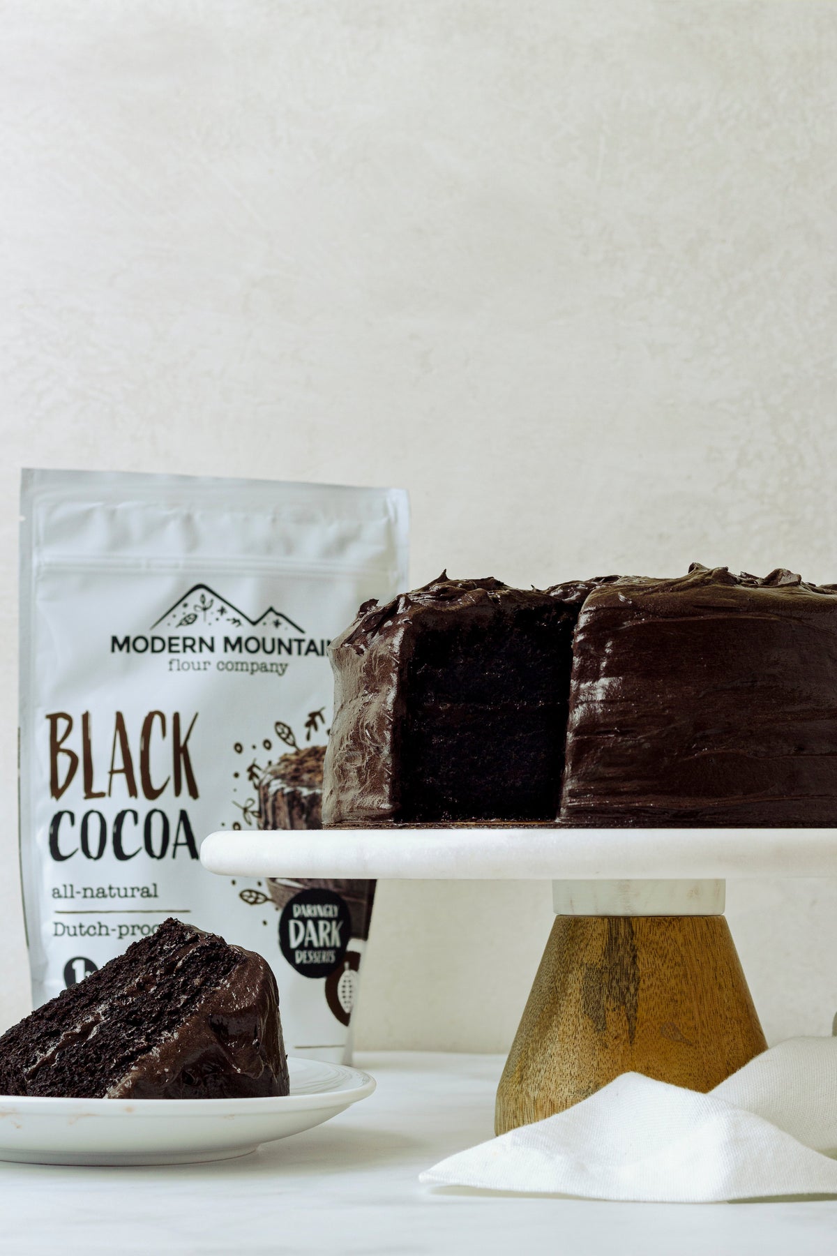 Modern Mountain Black Cocoa pouch beside a dark chocolate layer cake